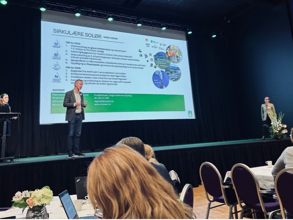 Presentasjon under Innlandsporteføljens hubsamling med to foredragsholdere på en scene foran et publikum, hvor lysbildet på skjermen viser mål og planer for Sirkulære Solør.
