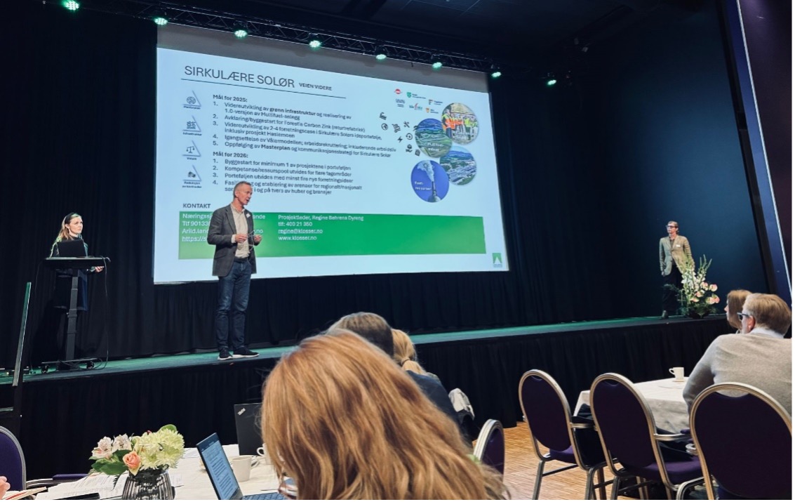 Presentasjon under Innlandsporteføljens hubsamling med to foredragsholdere på en scene foran et publikum, hvor lysbildet på skjermen viser mål og planer for Sirkulære Solør.